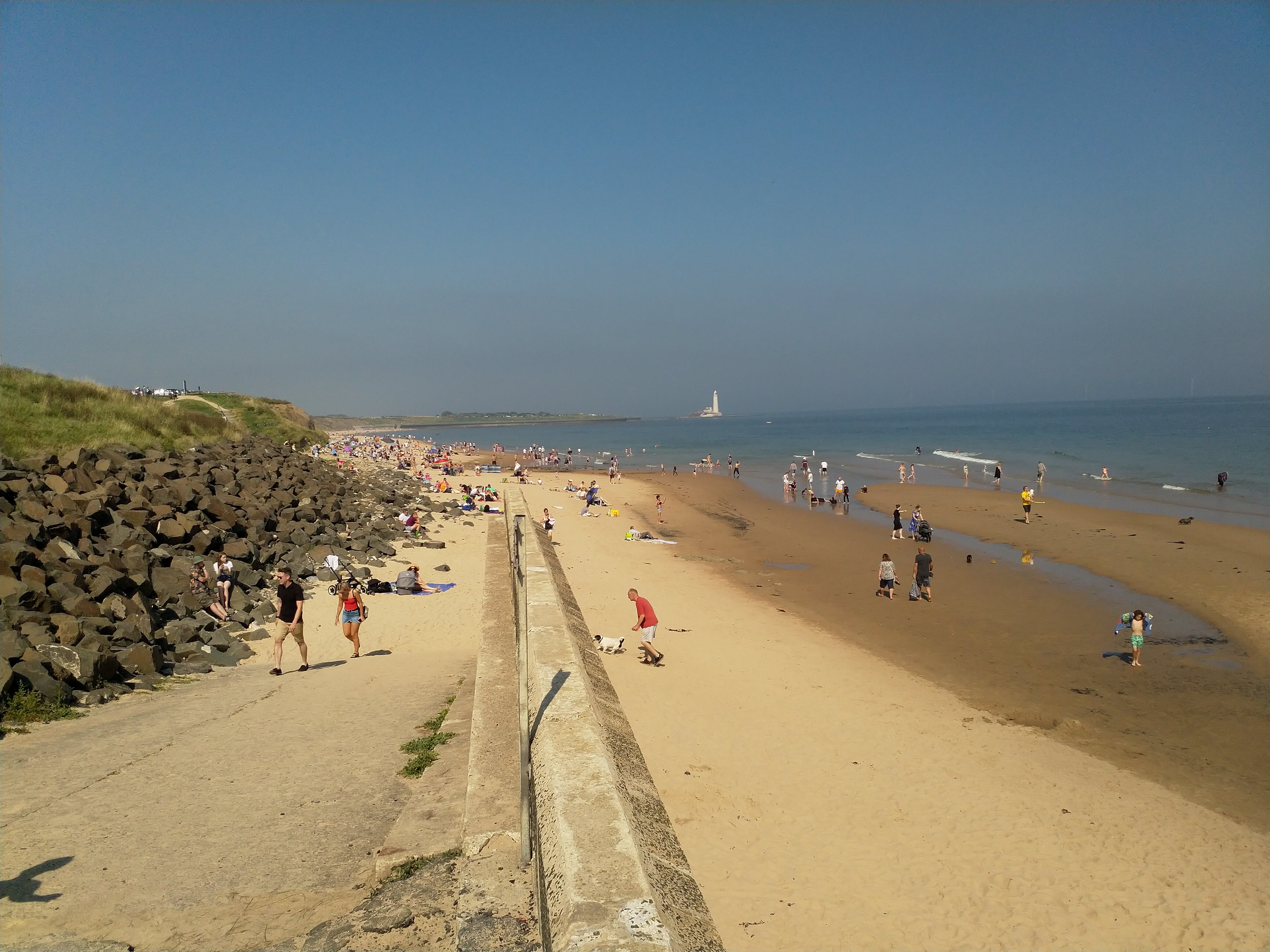 A beach crowded with people. There is a lighthouse in the far distance