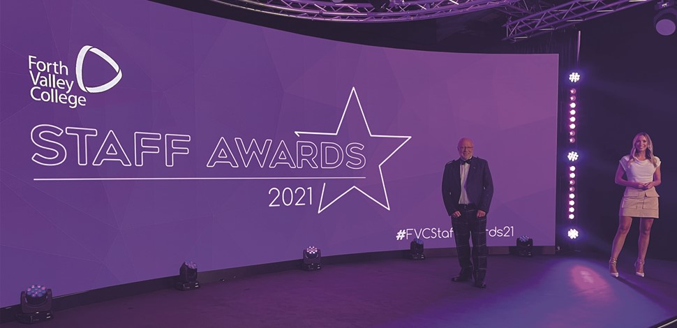 Two presenters stood on a stage in front of a sign reading "Forth Valley College Staff Awards 2021"